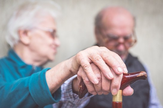 old couple with hands on walking cane