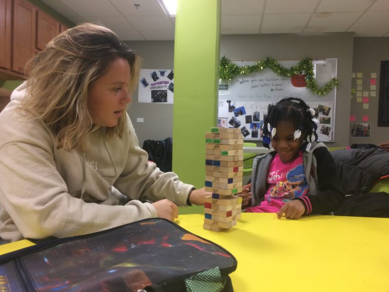 woman helping young girl play jenga blocks
