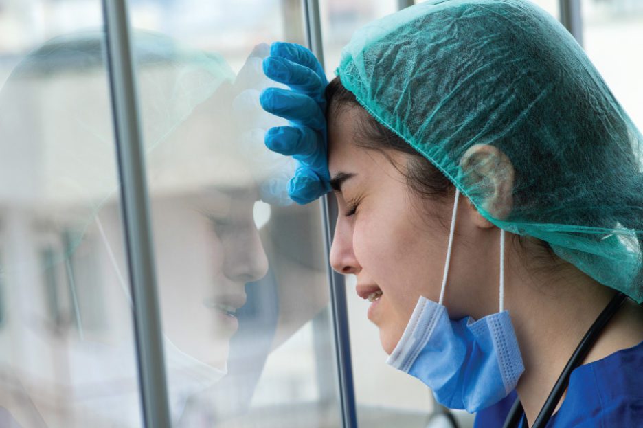 Nurse with mask lower cries near window.