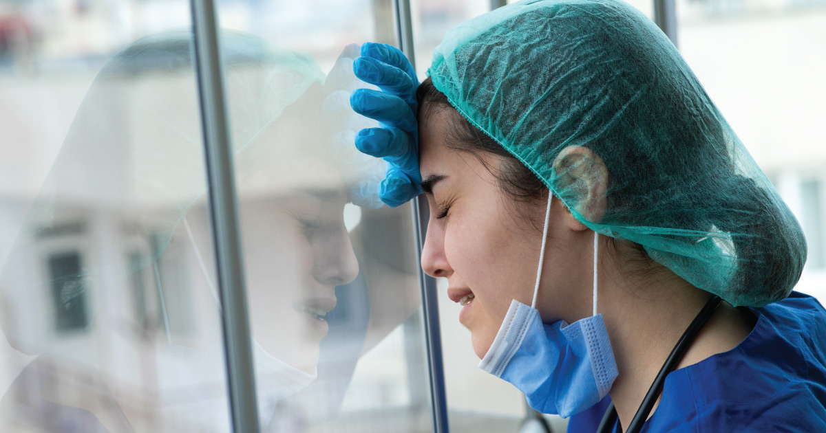Nurse with mask lower cries near window.
