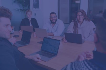 A diverse group of people sit with laptops at a conference table