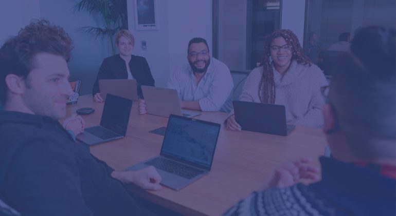 A diverse group of people sit with laptops at a conference table