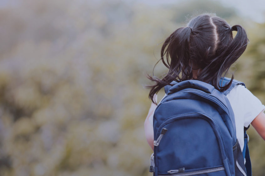 Image of a child running from behind while wearing a backpack.