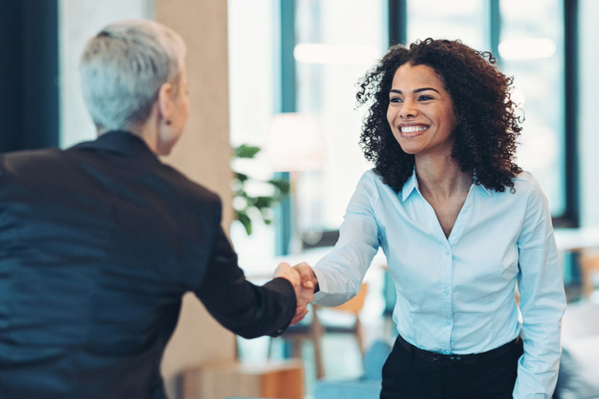 Image of two people shaking hands. One of them is smiling, while the other is viewed from behind.