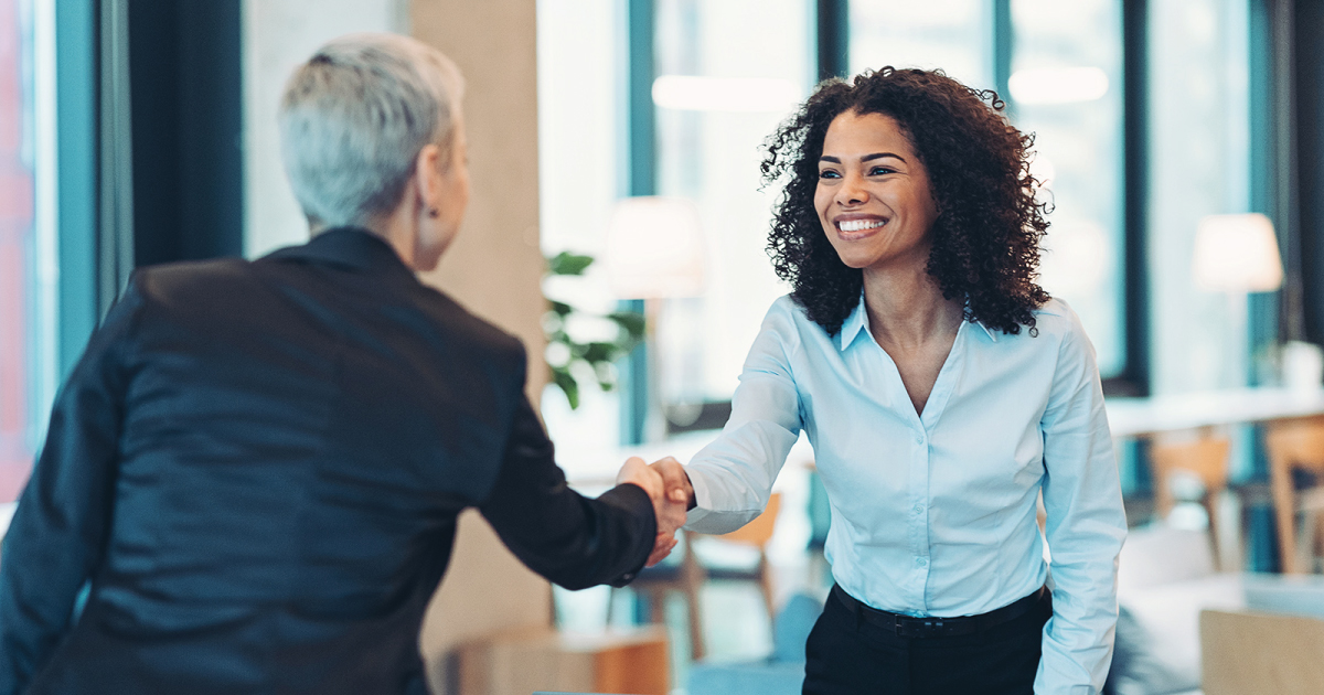 Image of two people shaking hands. One of them is smiling, while the other is viewed from behind.