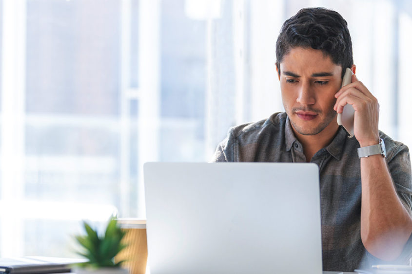 Photo of a man talking on the phone while typing on a laptop.
