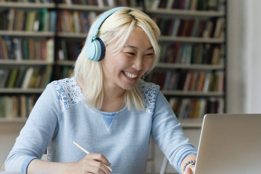 Photo of a woman wearing headphones smiling while using a laptop.