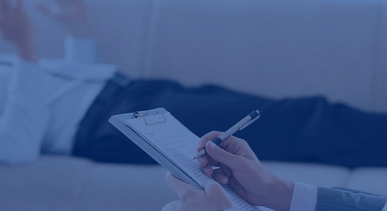 Patient lies on couch in background while therapist takes notes.