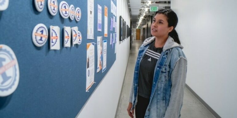 A young woman stands in a hallway looking at decorations on the wall.