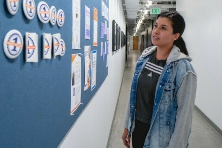 A young woman stands in a hallway looking at decorations on the wall.
