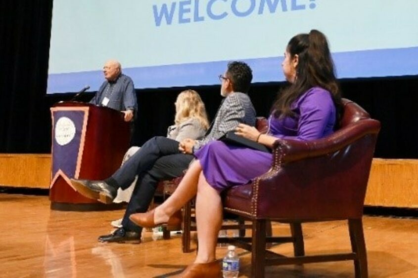 Participants in a talk about the Nation Ruth Cohen Institute populate a stage with a screen behind them displaying the name of the institute.