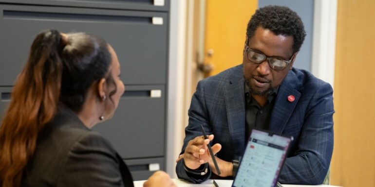A man and a woman engage in conversation while seated at a table in an office.