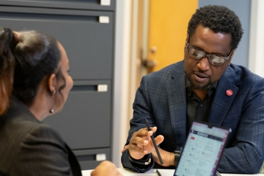 A man and a woman engage in conversation while seated at a table in an office.