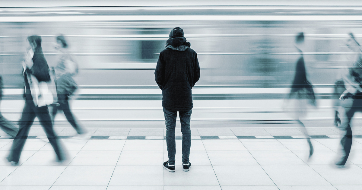Man standing on a subway platform with passing trains and pedestrians .
