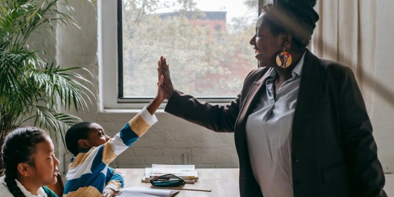 An elementary teaching high-fives a student while another student looks on.