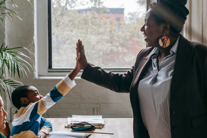 An elementary teaching high-fives a student while another student looks on.