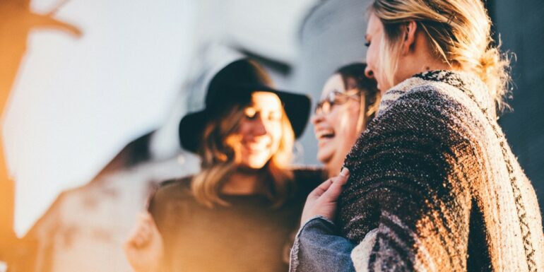 Three young women talk and laugh with each other in an out-of-focus mid-shot.