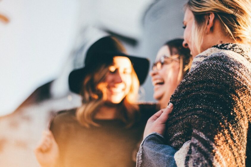 Three young women talk and laugh with each other in an out-of-focus mid-shot.