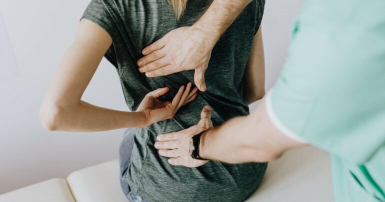 A doctor places their hands on a patient's back during a physical examination.