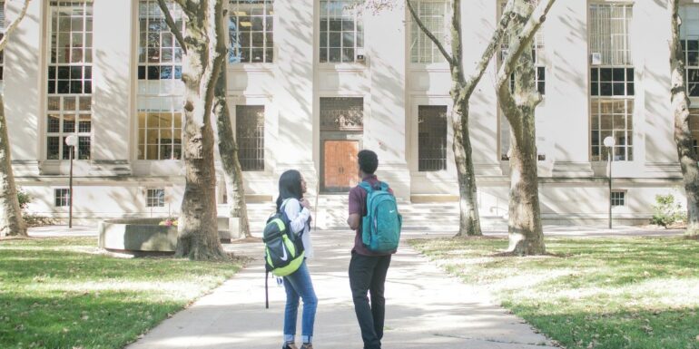 two students wearing backpacks outside a stone college building
