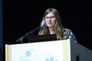 Woman with glasses speaking from a podium.