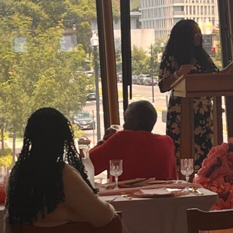 A woman speaks at a podium next to a window.
