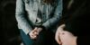A close-up of two people's folded hands as they sit next to each other