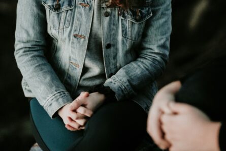 A close-up of two people's folded hands as they sit next to each other
