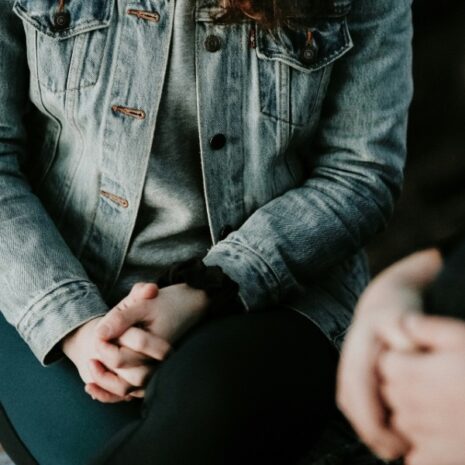 A close-up of two people's folded hands as they sit next to each other