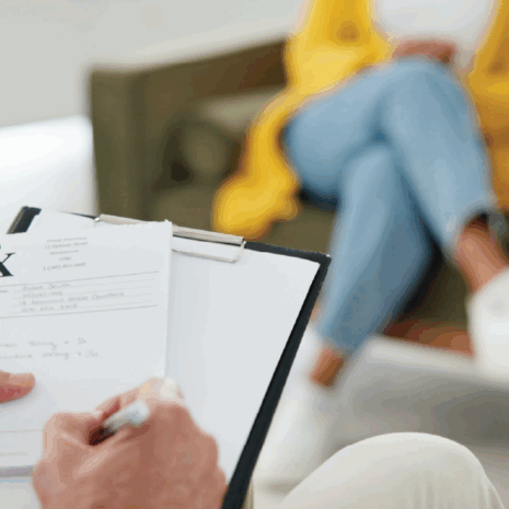 Close-up of man taking notes sitting across from a woman on couch with legs crossed.