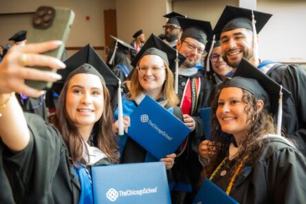 Newly graduated students from The Chicago School, wearing caps and gowns, pose for a group selfie holding their freshly issued diplomas.