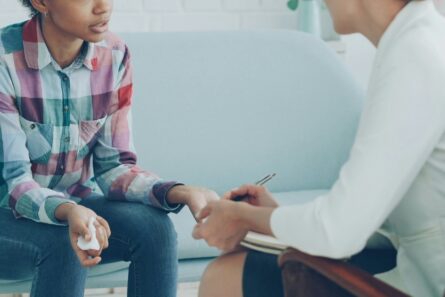 Two women sitting close and talking, One has a notepad.