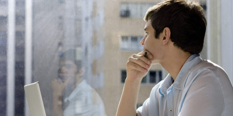 student with laptop looking out a window.