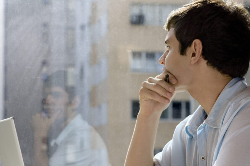 student with laptop looking out a window.
