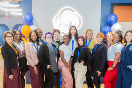 A group of adult students posing in front of the logo of The Chicago School.