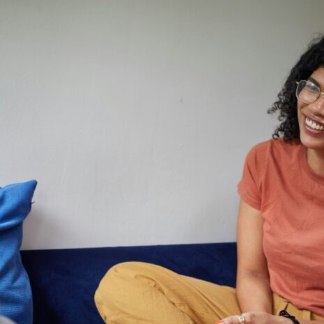 A woman with glasses laughing as she talks to a man.