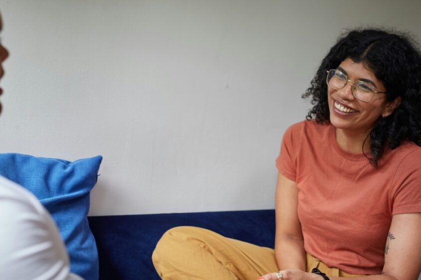 A woman with glasses laughing as she talks to a man.