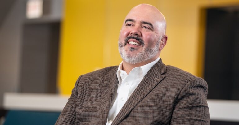 IllinoisCOM Founding Dean and Chief Academic Officer John Lucas, DO, smiles and looks off-camera into the middle distance.