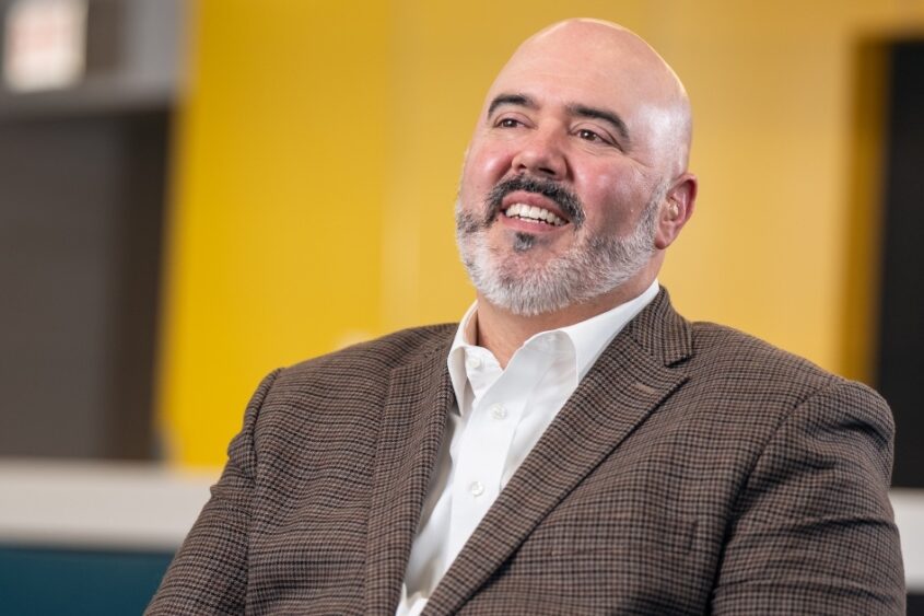 IllinoisCOM Founding Dean and Chief Academic Officer John Lucas, DO, smiles and looks off-camera into the middle distance.