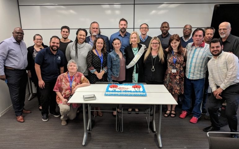 large group of people standing around a birthday cake