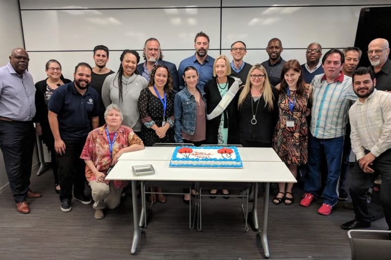large group of people standing around a birthday cake