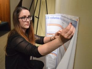 woman putting tacks into poster on wall