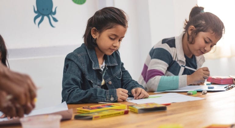 Two young girls drawing in a classroom.