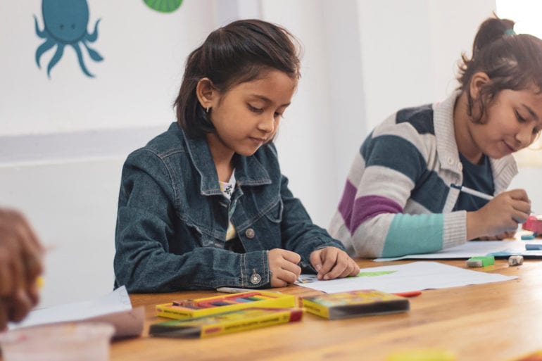 Two young girls drawing in a classroom.