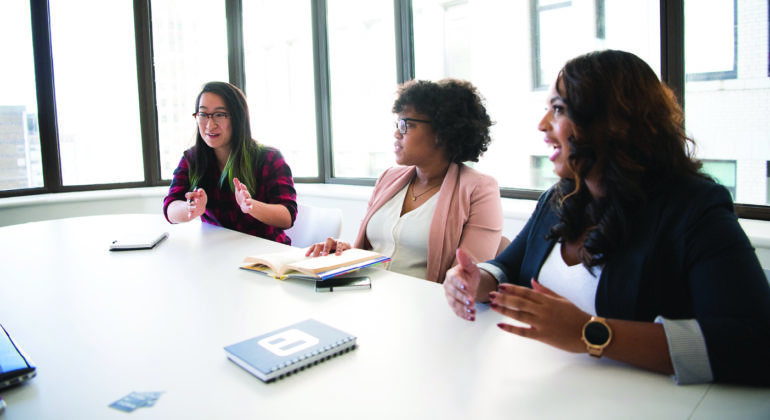 three women talking at long desk