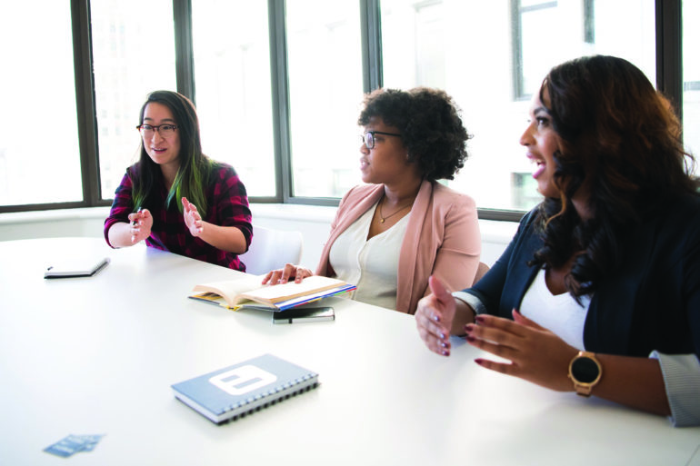 three women talking at long desk