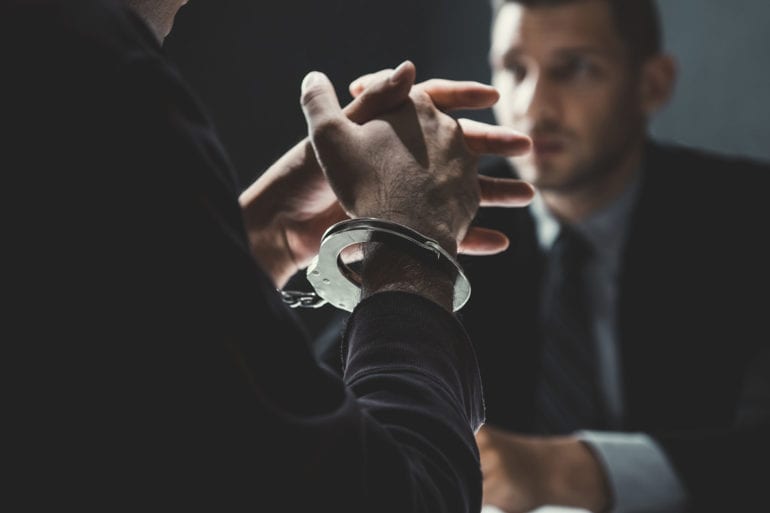 man in handcuffs speaking with lawyer