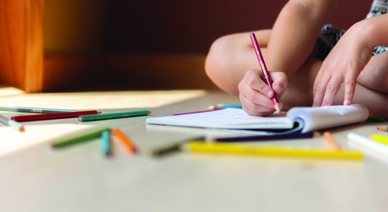 child writing in notebook with colored pencil