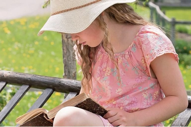 young girl reading a book on a bench