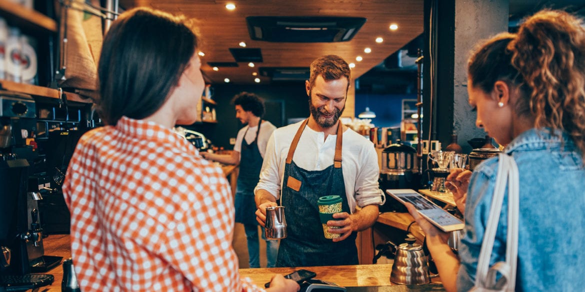 Two consumers in a coffee shop being served by a barista. This relates to the Starbucks company values example in this article.